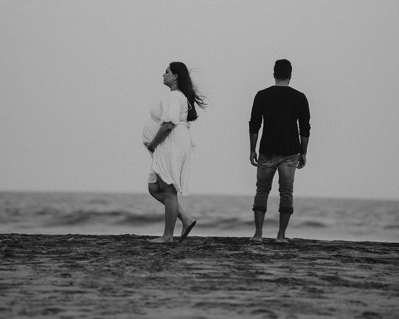 An expectant couple standing together by the sea